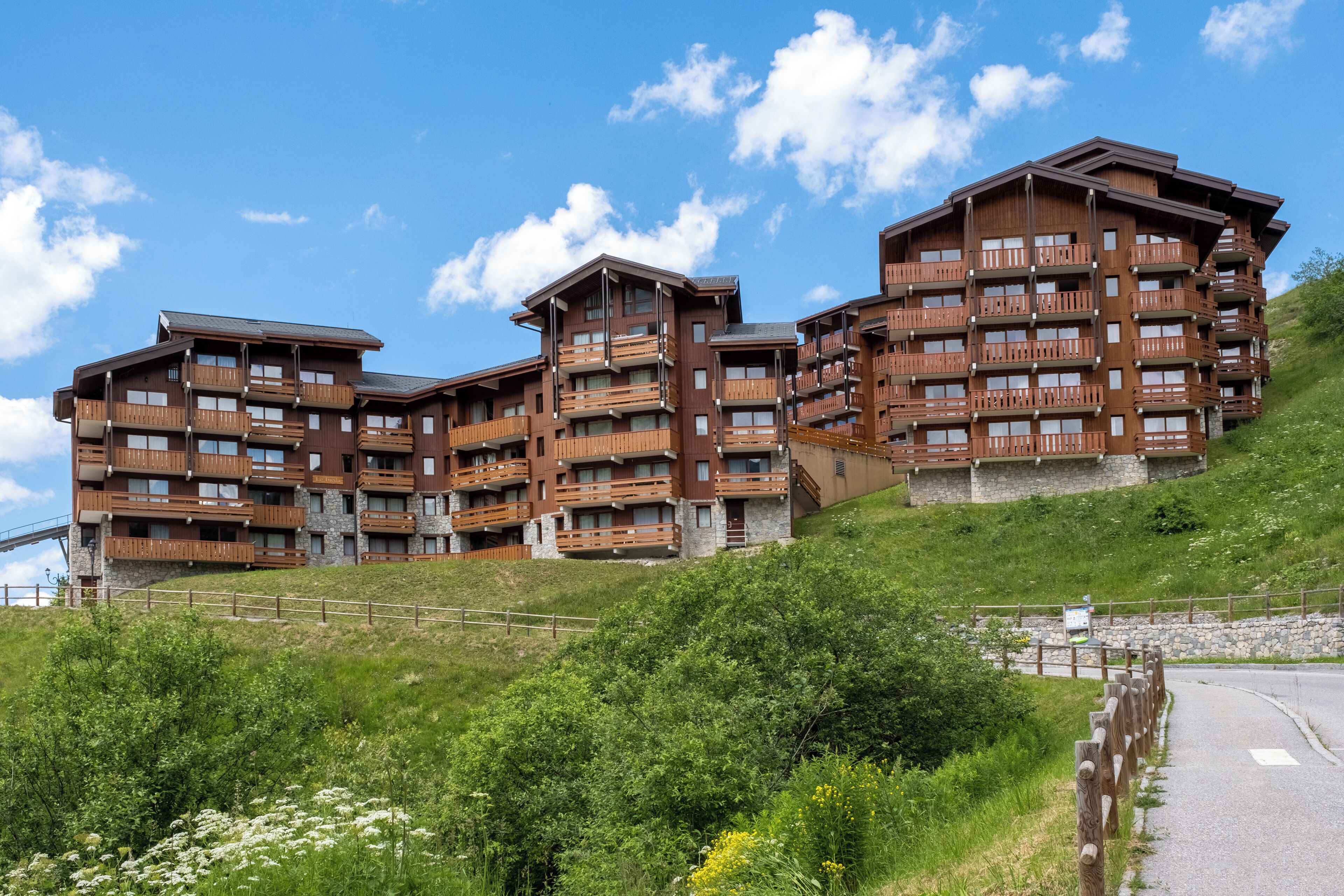 A multi-story hotel with balconies, situated on a hillside with a road in the foreground.