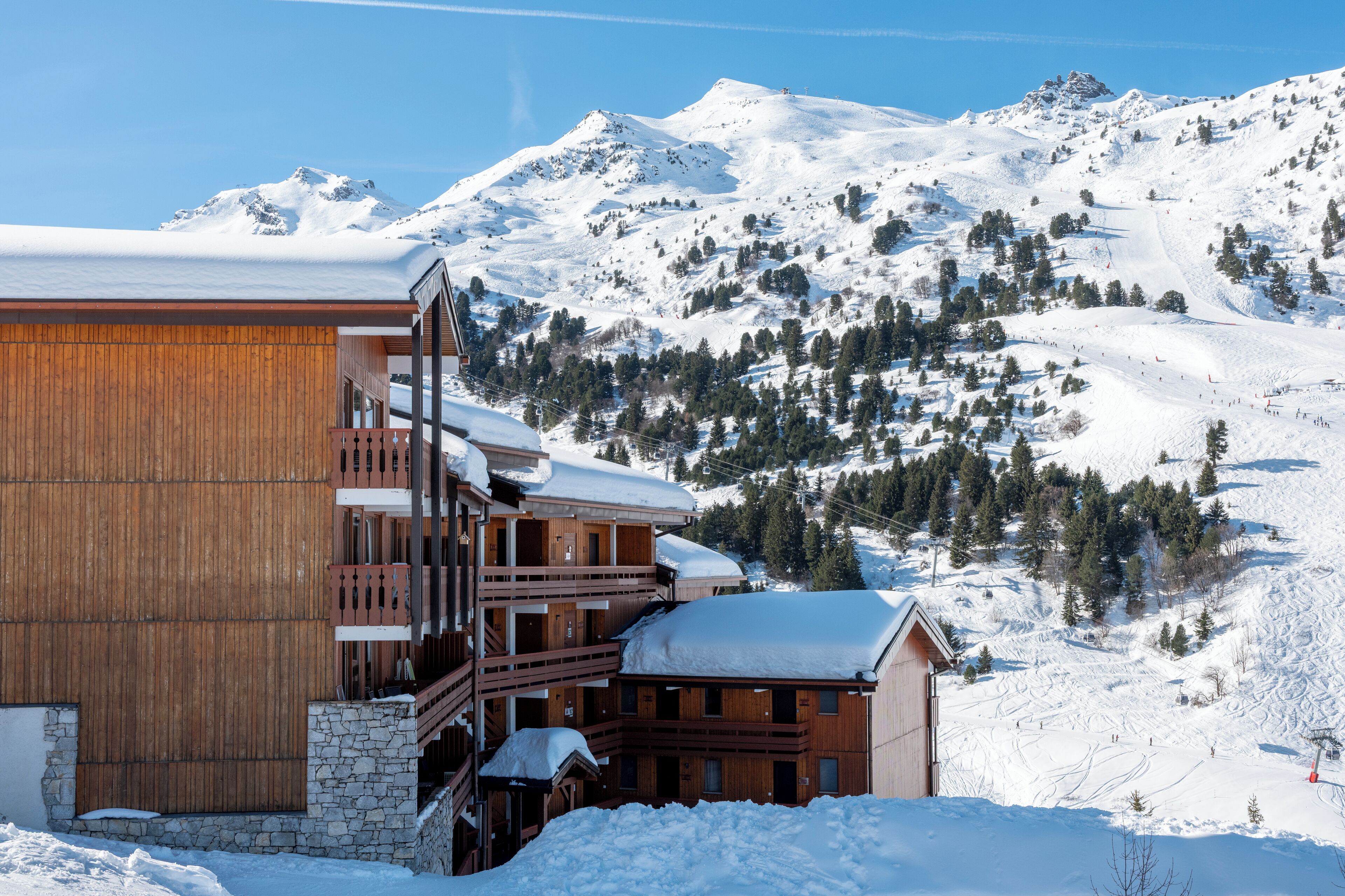Ein Holzbalkonbau, umgeben von schneebedeckten Bergen und Bäumen.