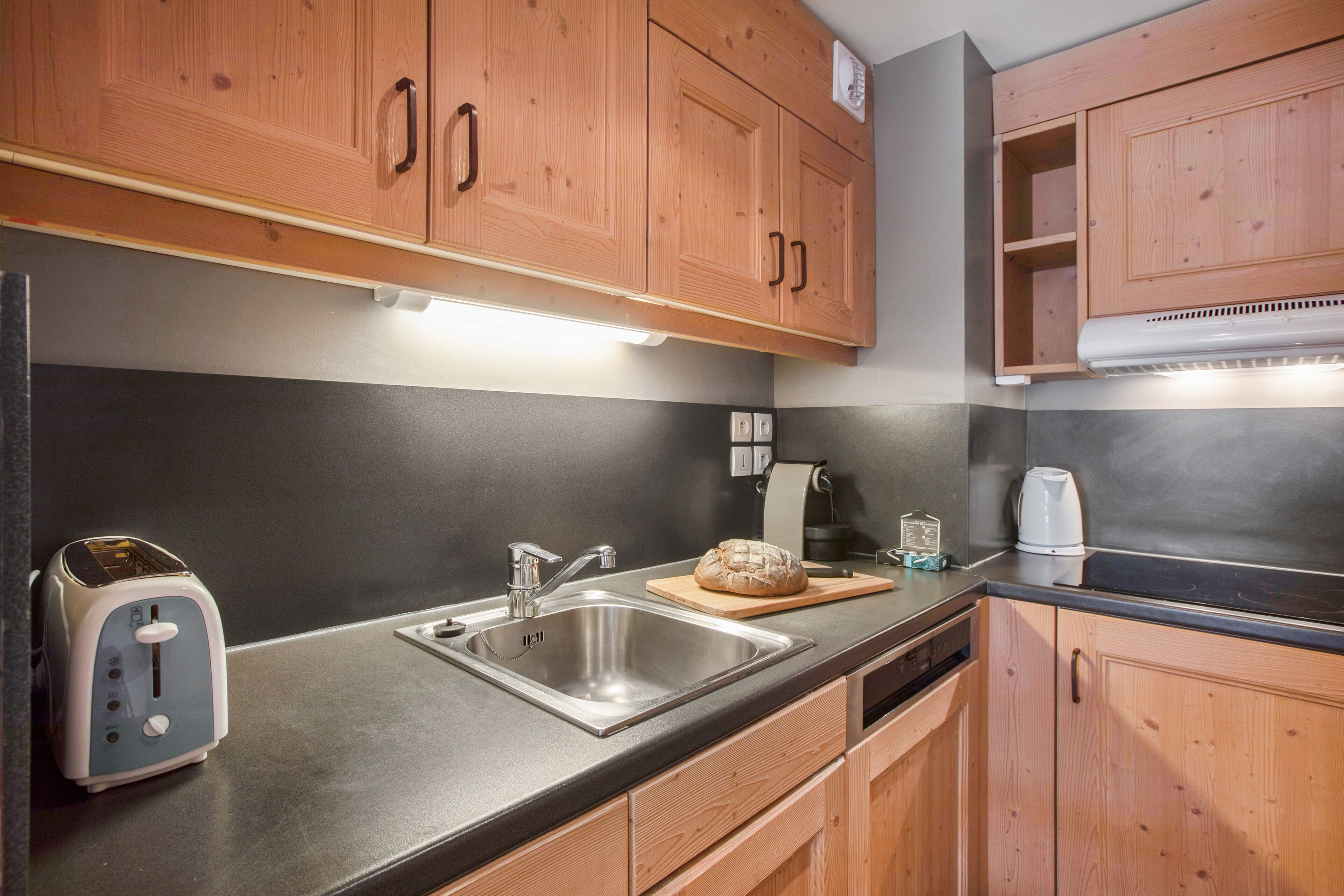 Una cocina moderna con armarios de madera, un lavamanos de acero inoxidable, un tostador y una tabla para pan.