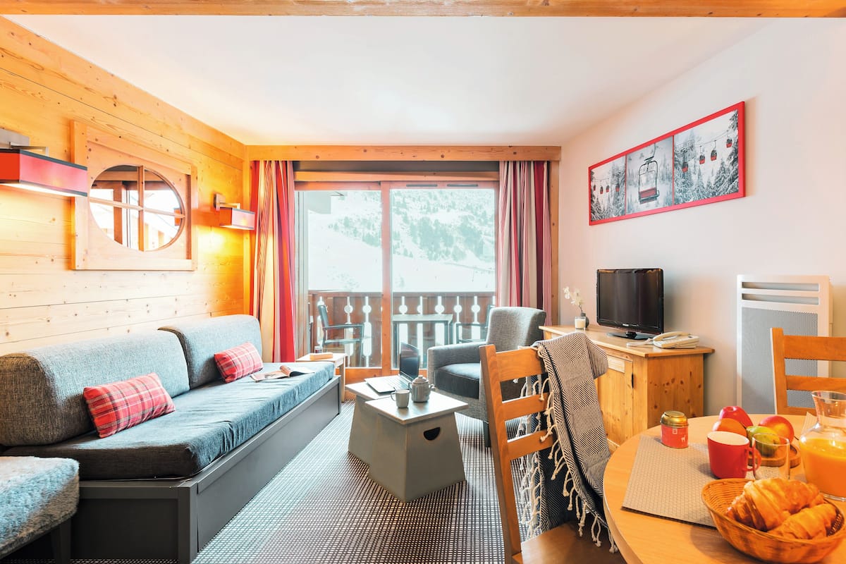 Une pièce confortable avec un canapé, une petite table avec une bouilloire, une chaise, un téléviseur et un coin petit-déjeuner avec des fruits et un panier.