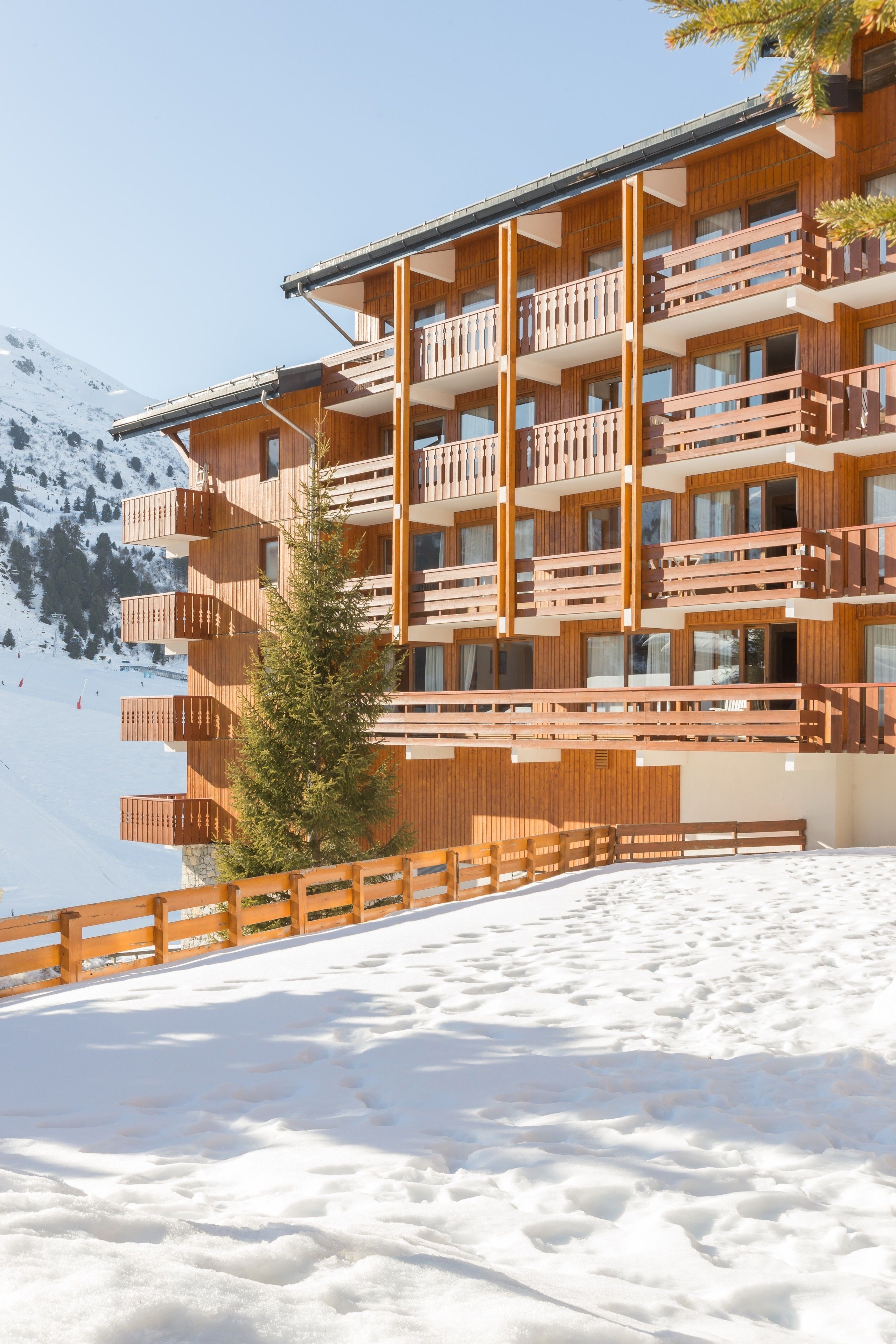 A multi-story wooden building with balconies, set against a snowy mountain backdrop.