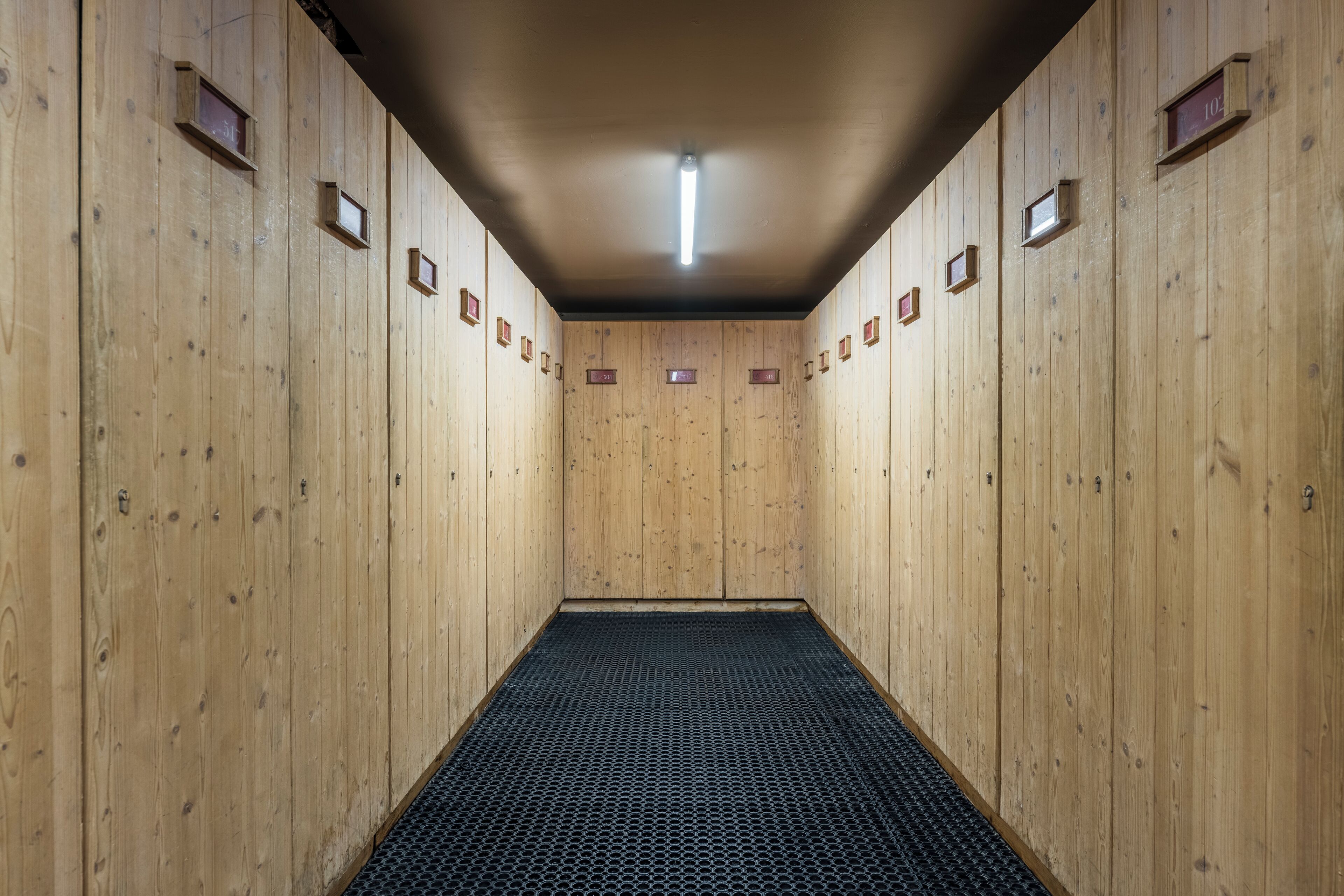 A wooden interior with a central black mat, wooden walls, and numbered lockers.