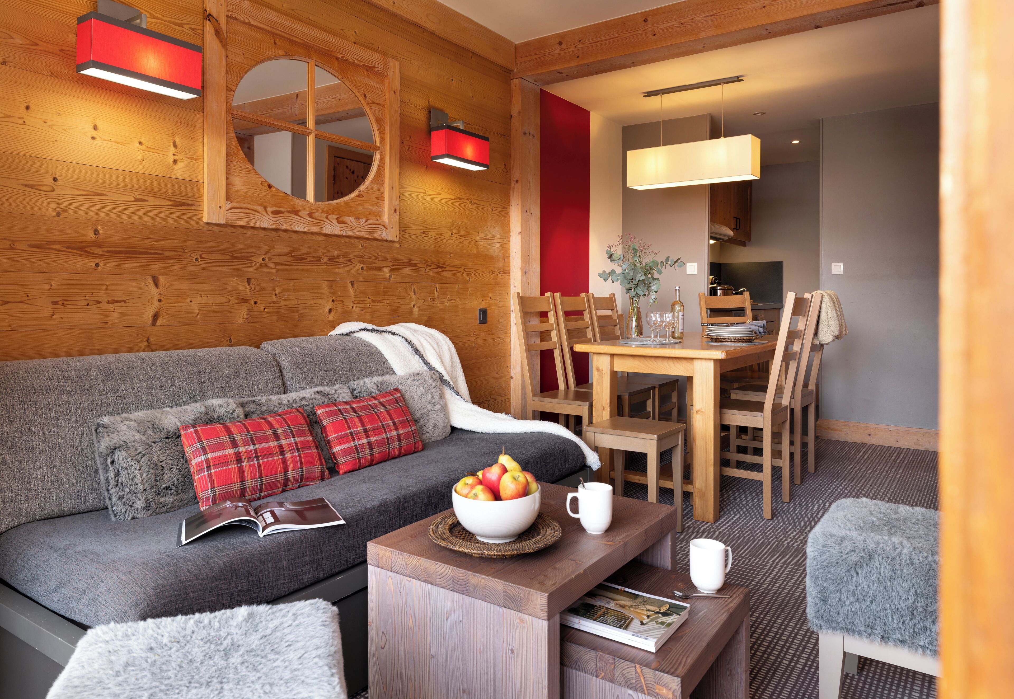 A cozy room with a sofa, a dining table, and chairs. There is a bowl of fruit on the table and a book on the sofa.