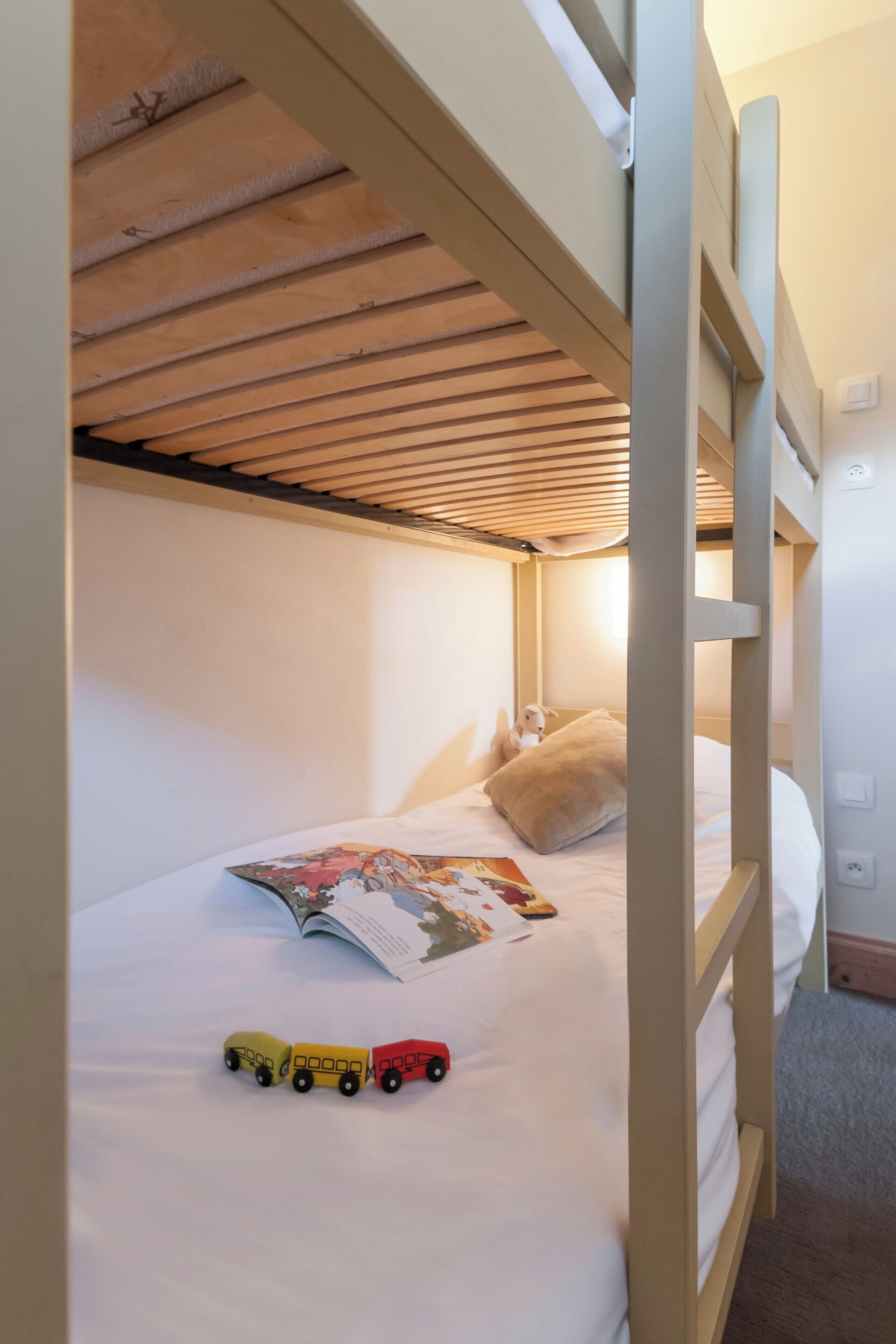 A bunk bed with a wooden ceiling and a single bed with a pillow and a book.