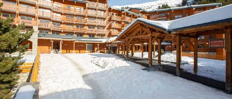 Ein mehrstöckiges Holzgebäude mit Balkonen, einem überdachten Außenbereich und einem mit Schnee bedeckten Gelände.