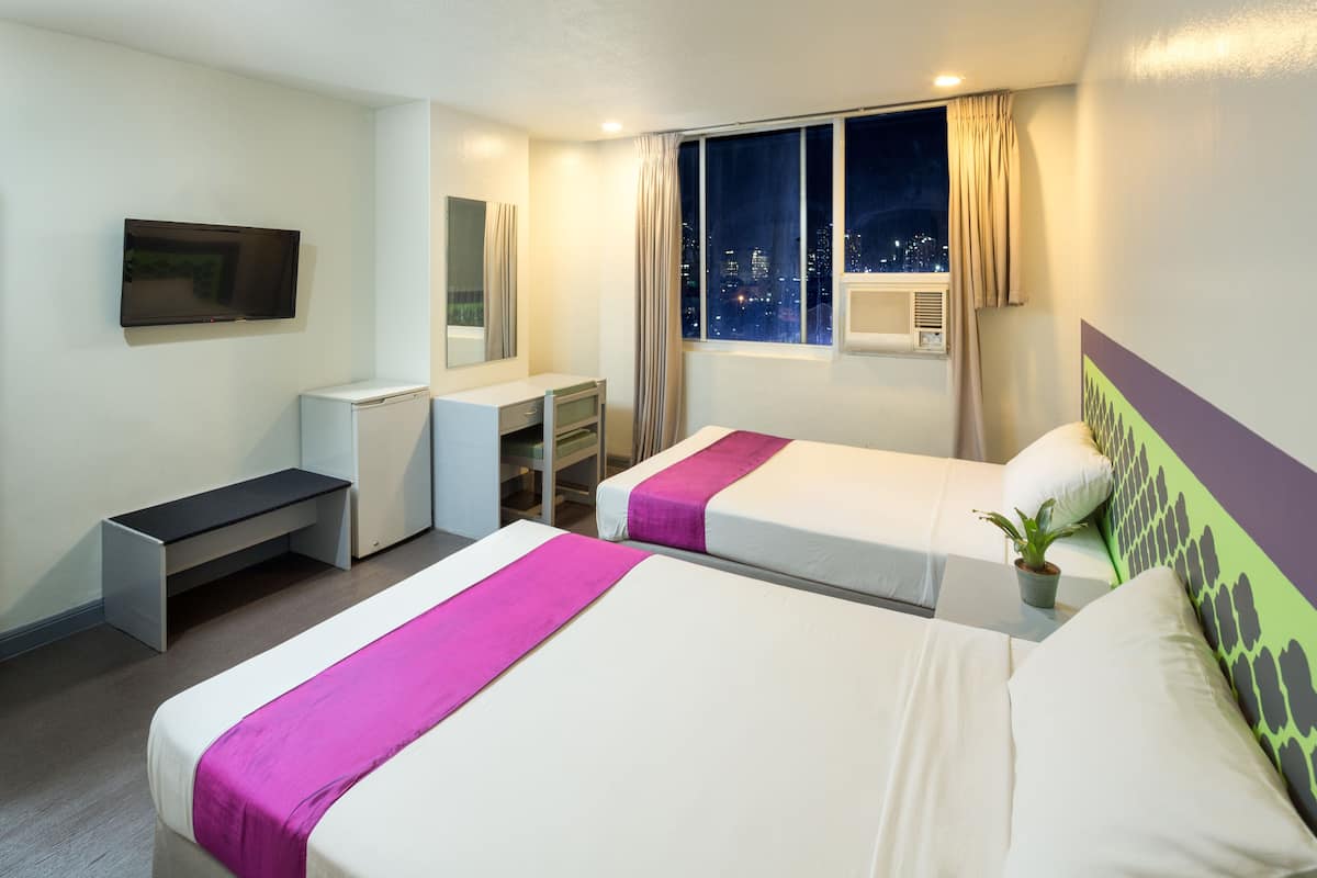 Une chambre d’hôtel avec deux lits, un bureau, une télévision et une fenêtre donnant sur la ville.