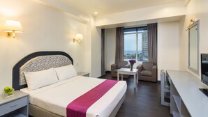 Habitación de hotel con una cama grande, un escritorio, dos sillas, un televisor y vistas a la ciudad.