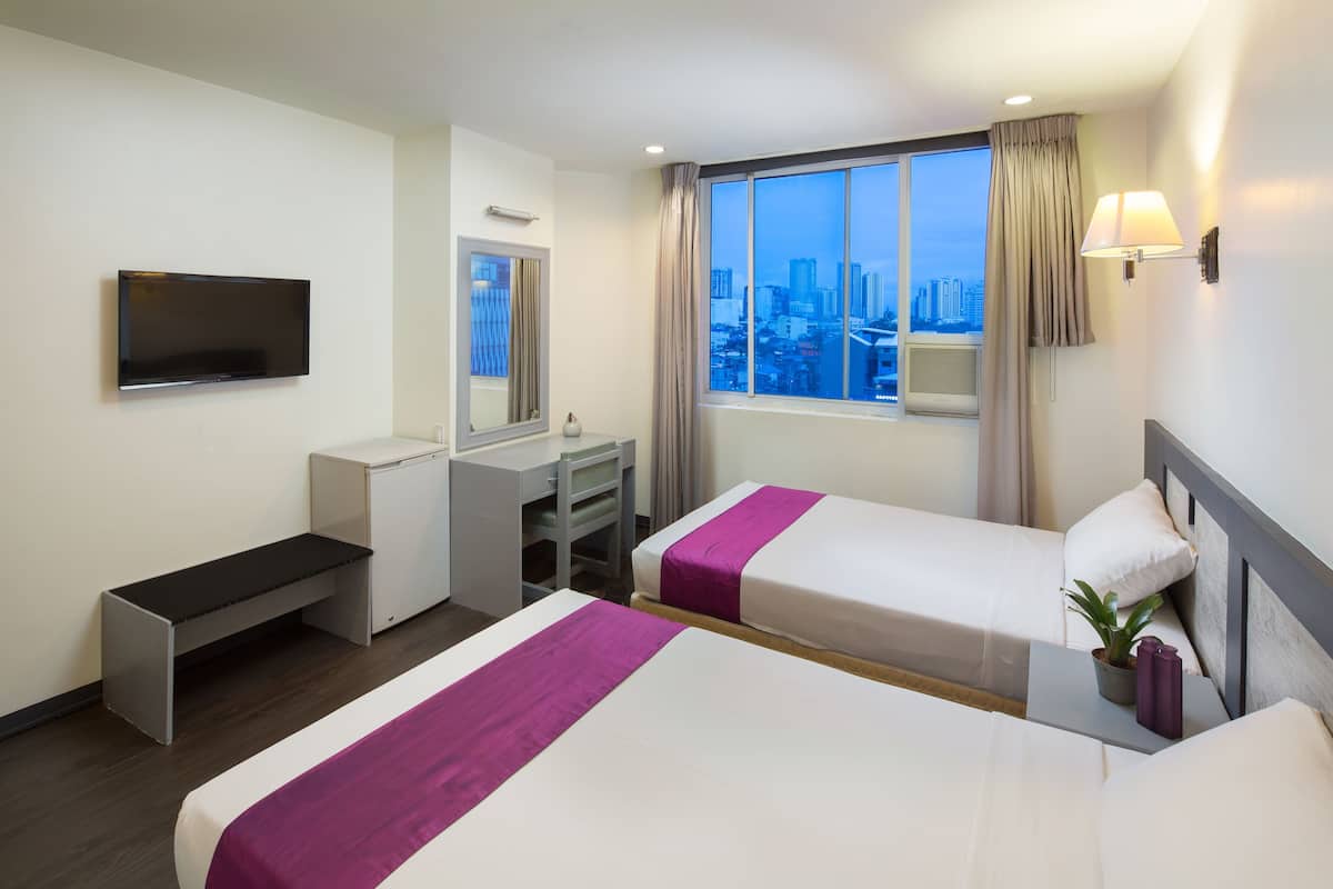 Une chambre d’hôtel avec deux lits, un bureau, une télévision, une fenêtre donnant sur la ville et une lampe.