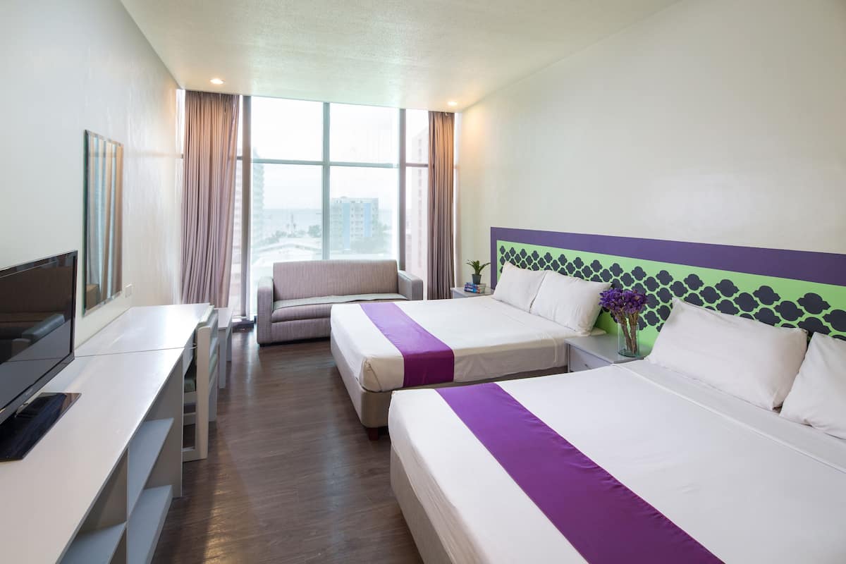 Une chambre d’hôtel avec deux lits, un bureau avec une télévision, une fenêtre avec des rideaux et une vue sur les immebles.