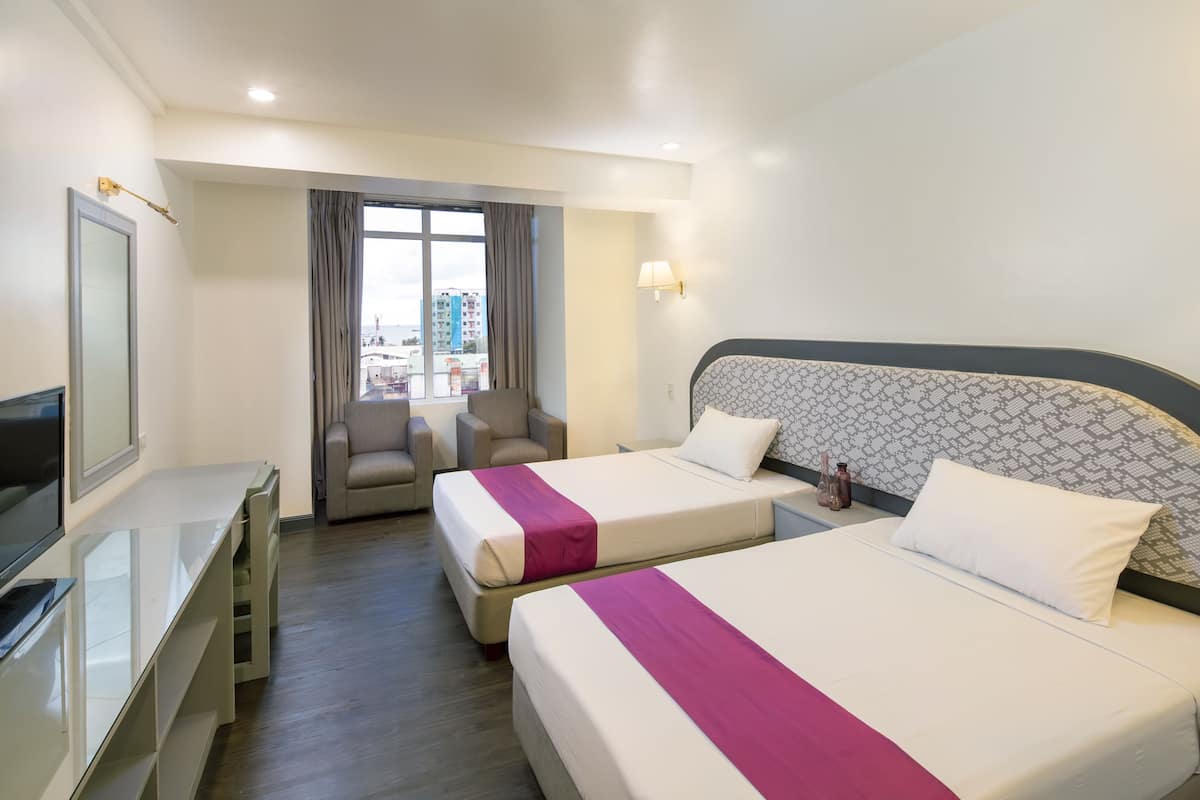 Une chambre d’hôtel avec deux lits, un bureau, une chaise, une télévision et une fenêtre donnant sur la ville.