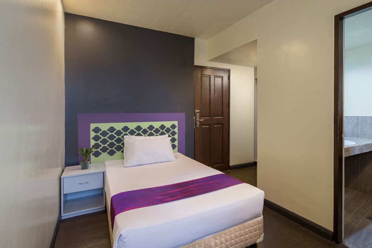 Une chambre d’hôtel avec un lit, une table de chevet, une porte et une salle de bain visible à travers une porte ouverte.