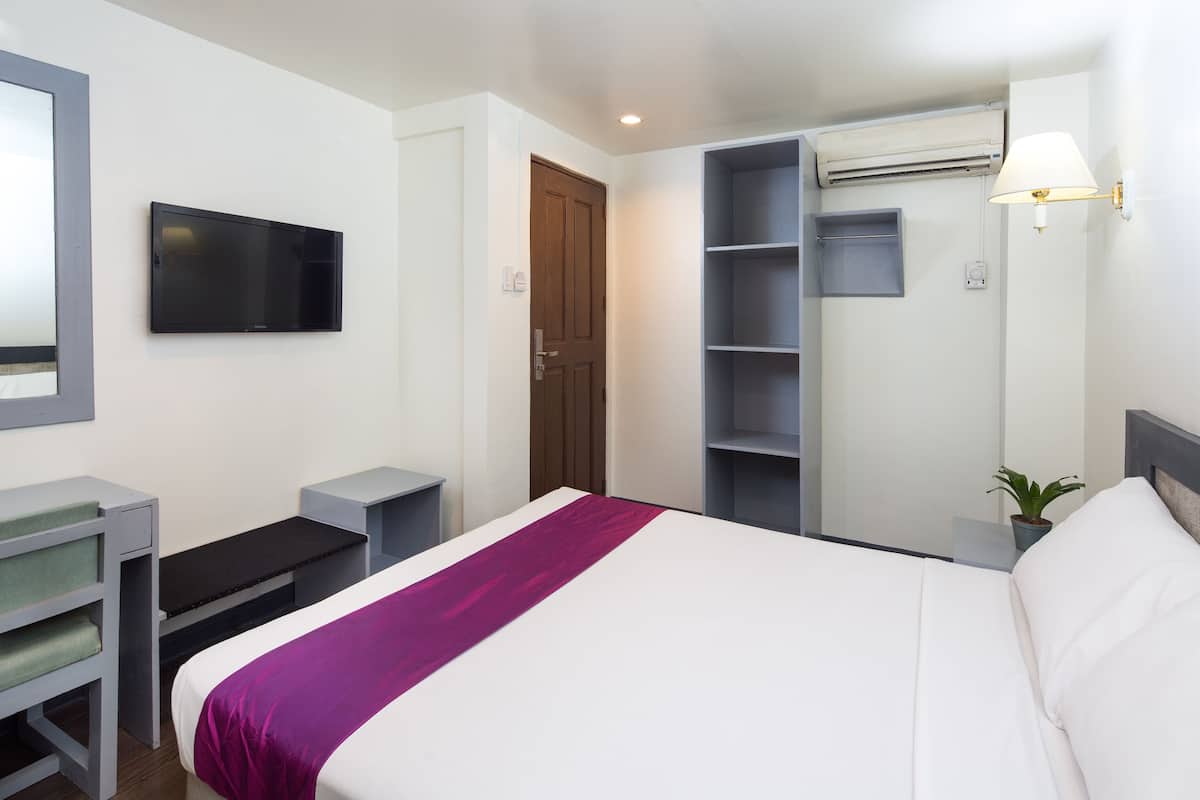 Une chambre d’hôtel avec un lit, un téléviseur fixé au mur, un bureau, une étagère et une plante en pot.