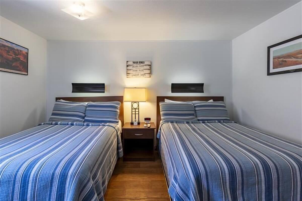 A room with two beds, a nightstand with a lamp, and a wall sign.