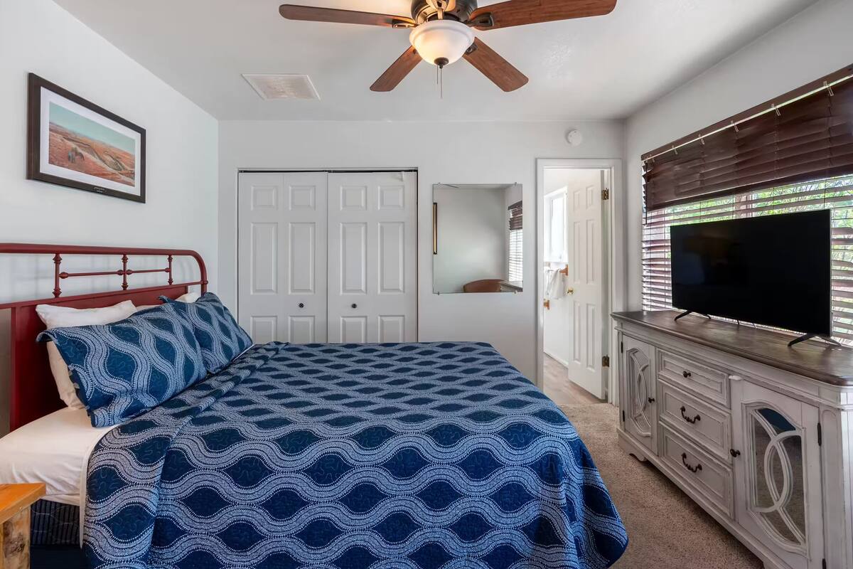 A bedroom with a bed, a ceiling fan, a dresser, a television, and a door.