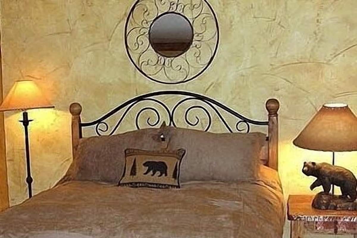Una cama con estructura de madera, un cojín con motivos de oso, un espejo adosado a la pared y dos lámparas de noche.
