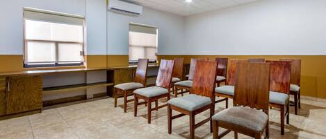 A conference room with wooden chairs and a long table, air conditioning units on the walls, and a tiled floor.