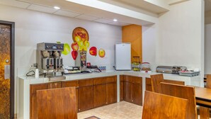 Une cuisine moderne équipée d’une machine à café, d’un réfrigérateur et d’une fresque murale sur le thème des fruits.