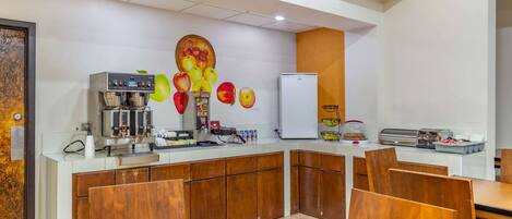 Una cocina moderna con cafetera, refrigerador y un mural temático de frutas.