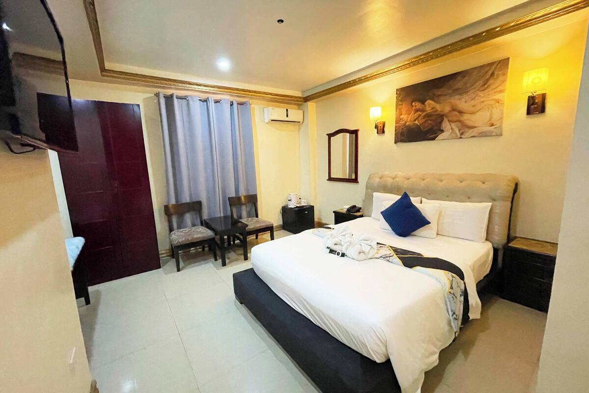 A hotel room with a bed, bedside table, chair, and a TV.