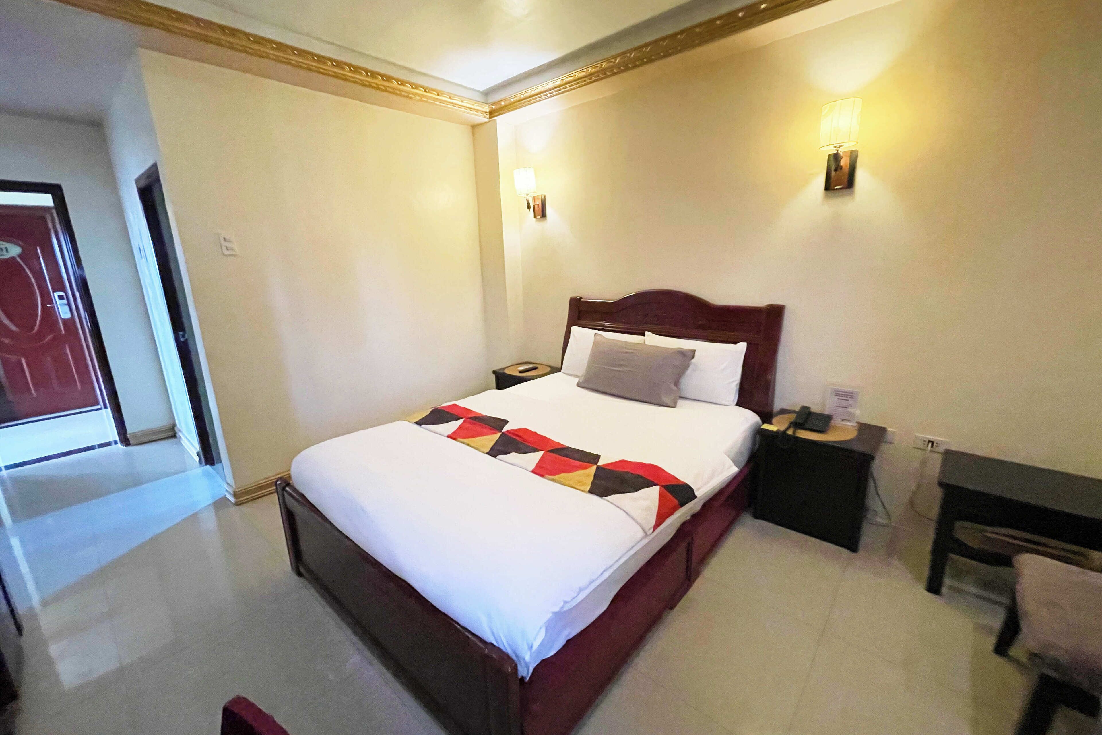 A hotel room with a large bed, a bedside table, a nightstand, a lamp, and a chair.