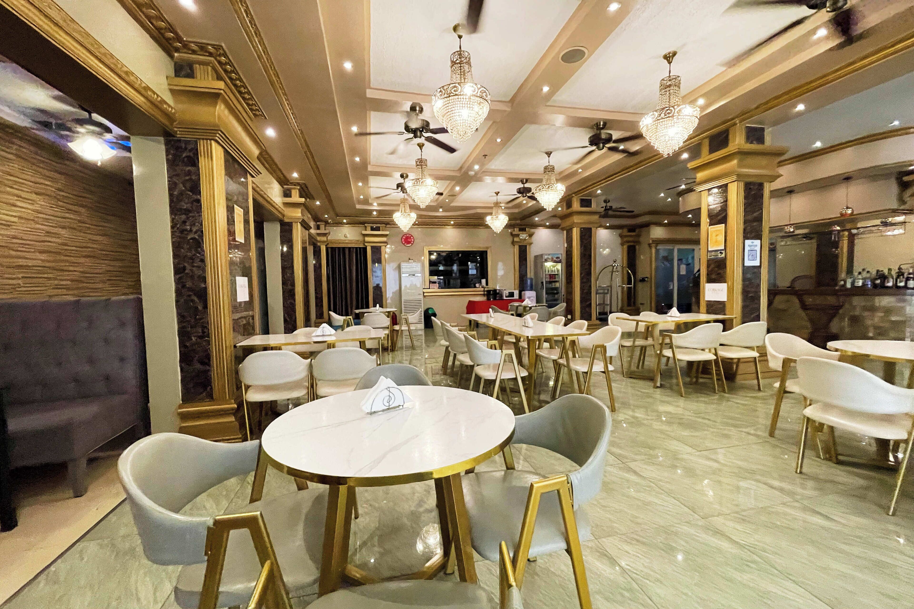 A spacious dining area with round tables and chairs, ceiling fans, and chandeliers.