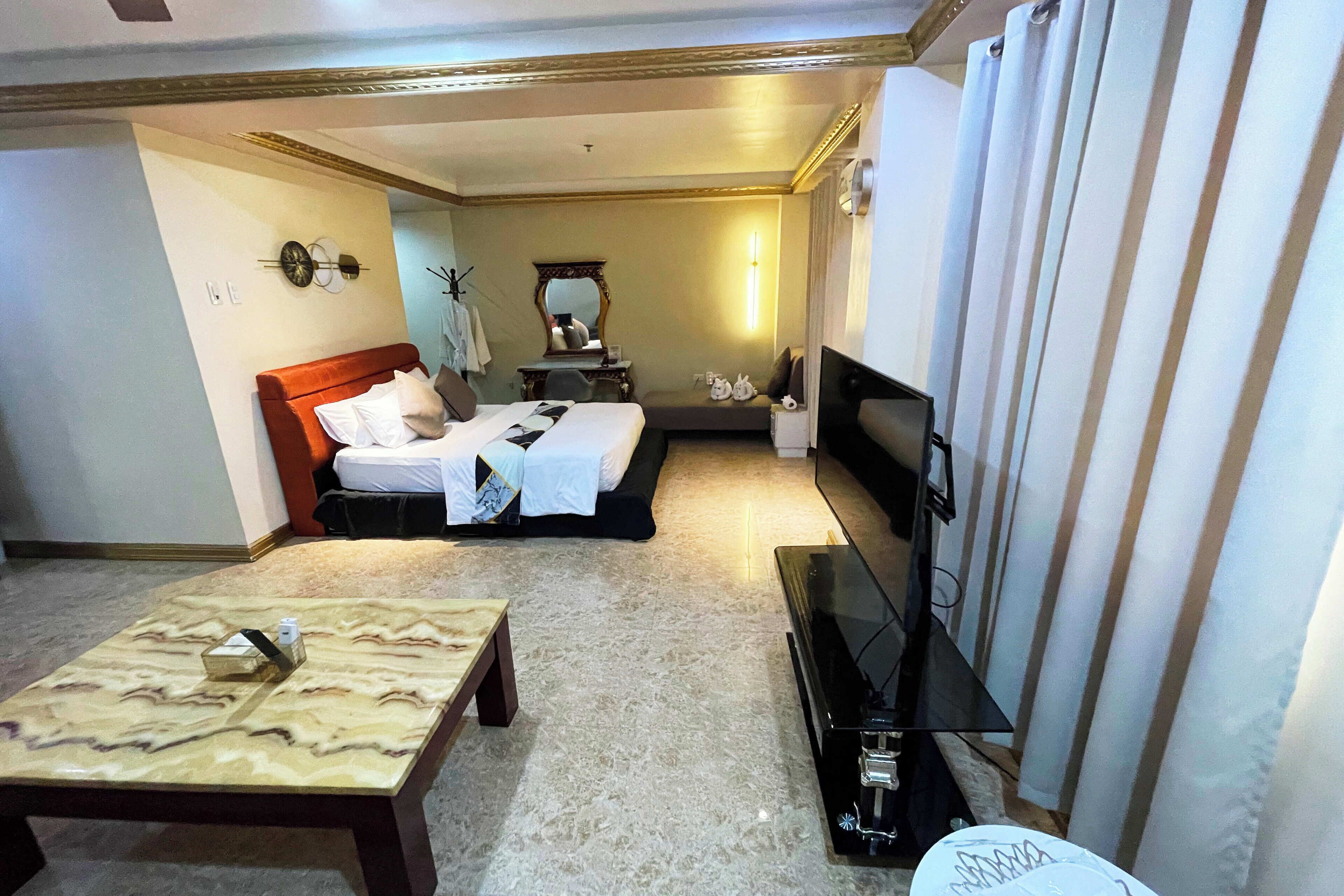 A hotel room with a bed, a TV, a coffee table, and a desk with a chair.