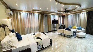 Una habitación de hotel con cama, sofá, televisor y ventilador de techo.