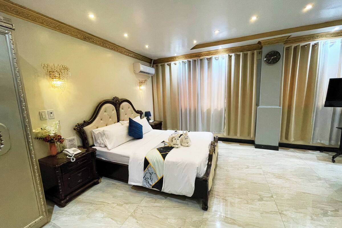 A well-appointed hotel room with a large bed, a nightstand with a phone, a wall-mounted clock, and a television.