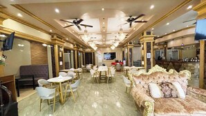 Un vestíbulo de hotel con zona de comedor central, sofás y una pantalla de televisión.