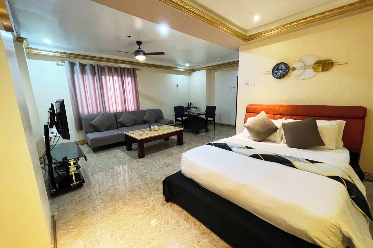 A hotel room with a bed, a sofa, a coffee table, a TV, and a ceiling fan.