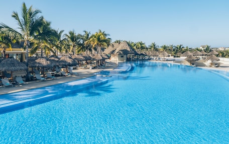A large, clear swimming pool with lounge chairs and palm trees.