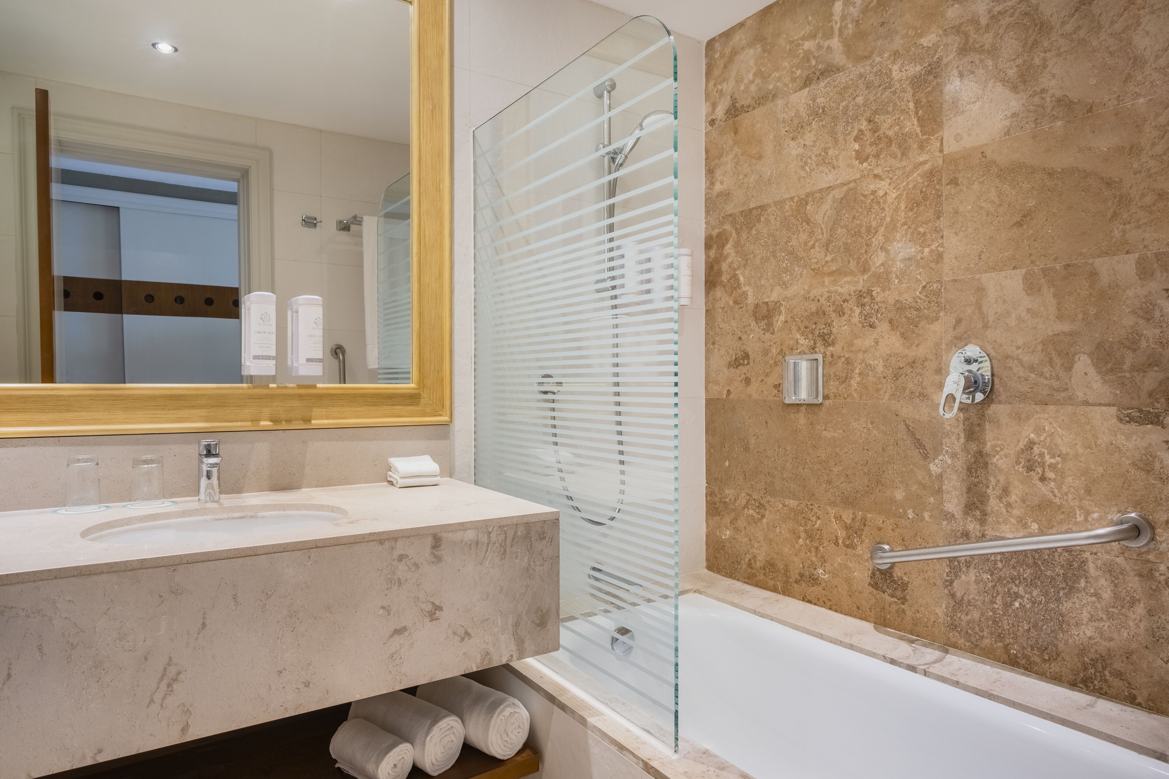 A modern bathroom with a marble sink, glass shower enclosure, and a bathtub with a grab bar.