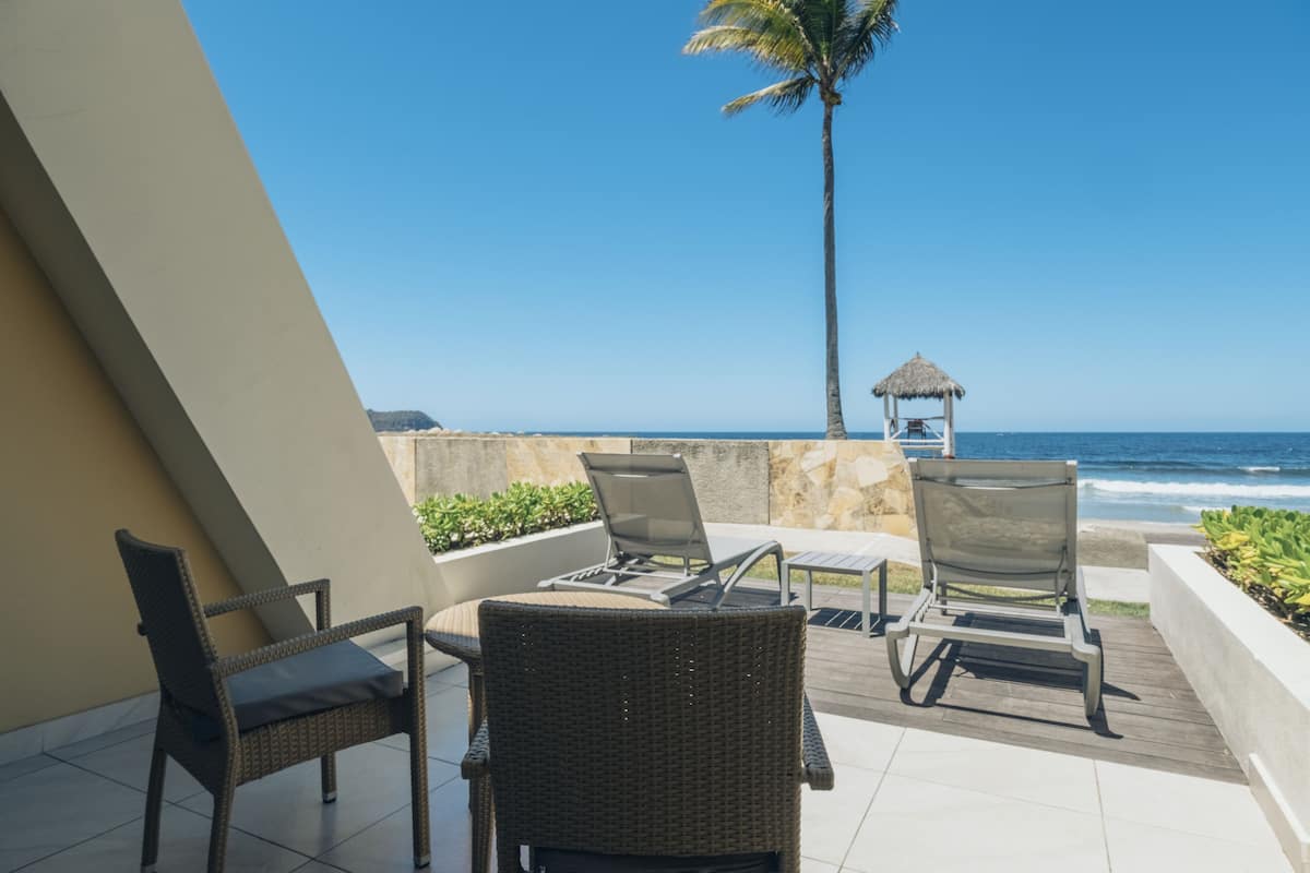 A balcony with wicker chairs and a thatched-roof structure overlooking the ocean.