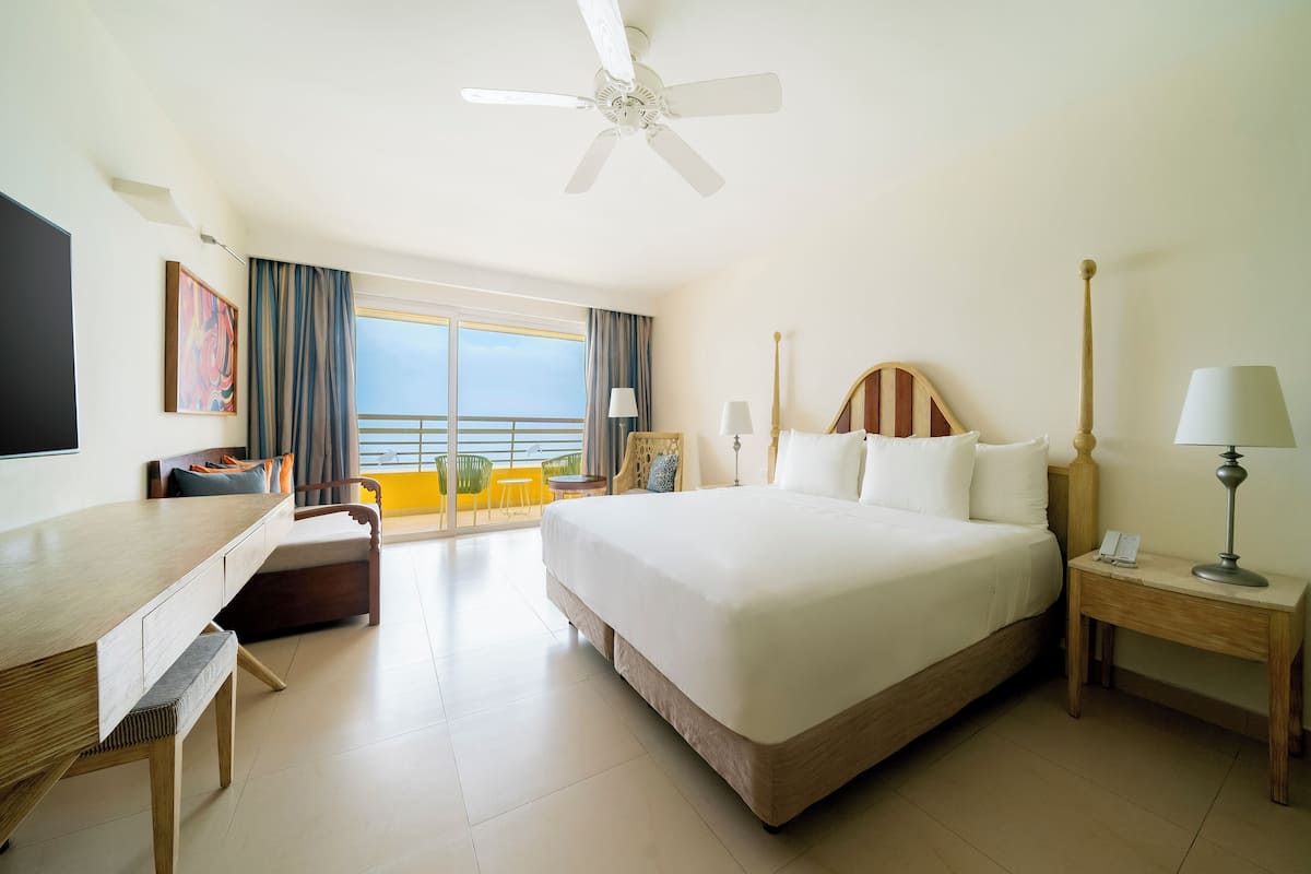 A hotel room with a bed, a desk, a chair, a nightstand, and a ceiling fan.