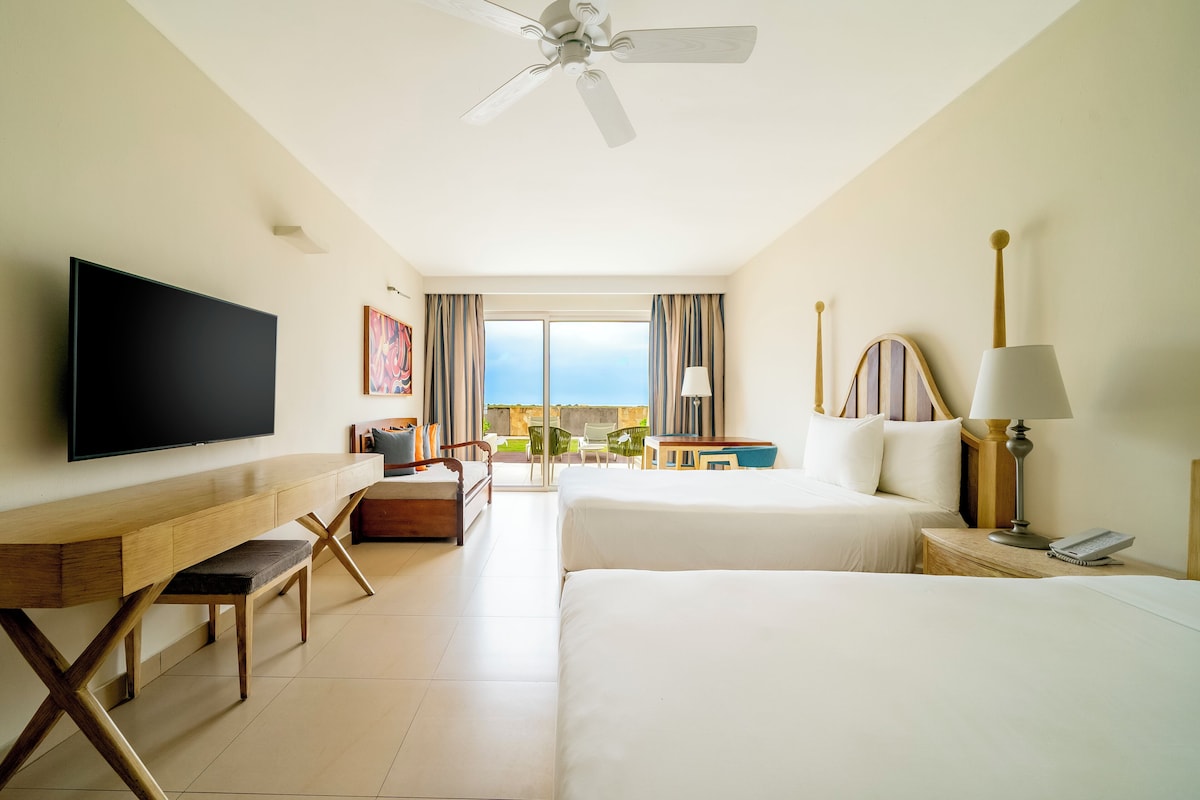 A hotel room with a bed, a desk, a TV, a lamp, and a view of the outdoors. - Iberostar Selection Playa Mita - All Inclusive (Punta de Mita)
