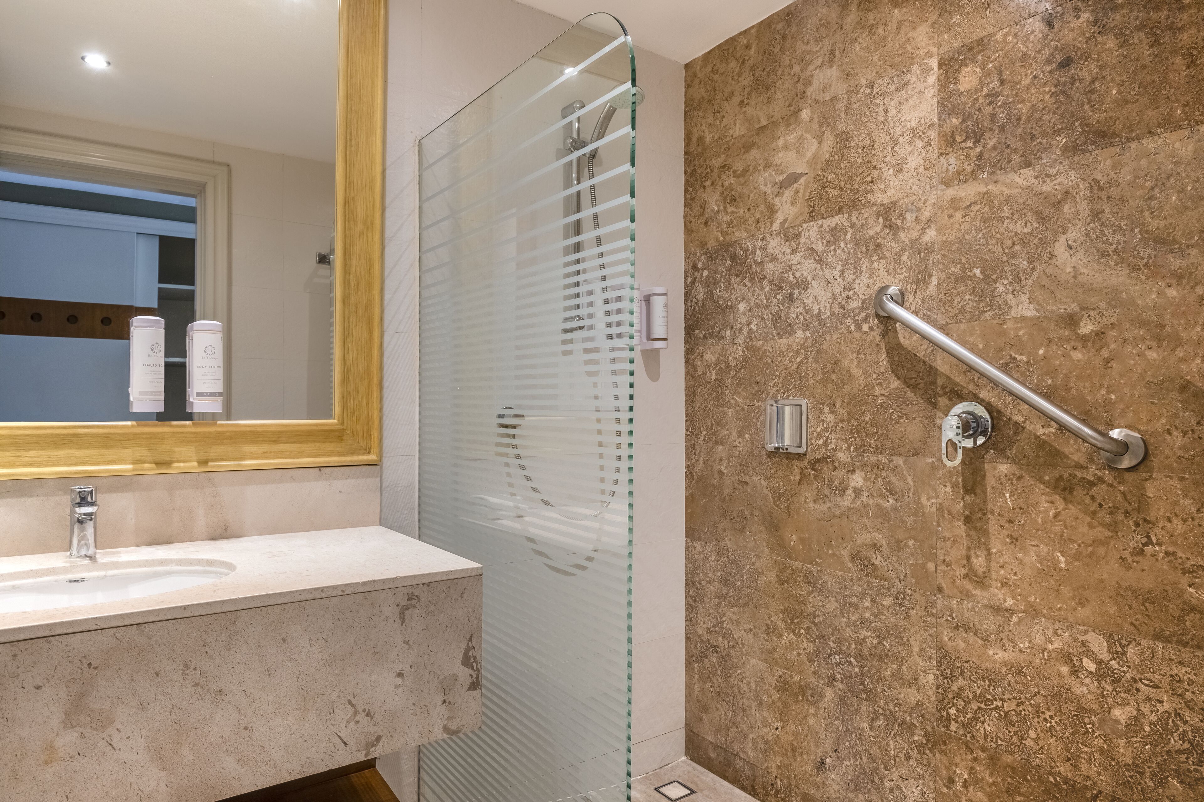 A modern bathroom with a glass shower enclosure, a vanity with a sink, and a handrail for accessibility.