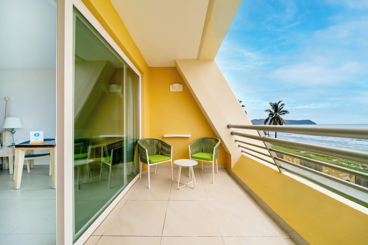 A balcony with a glass door, two green chairs, a small table, and a view of the ocean.