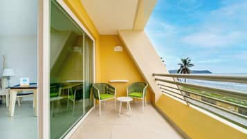 A balcony with a glass door, two green chairs, a small table, and a view of the ocean.