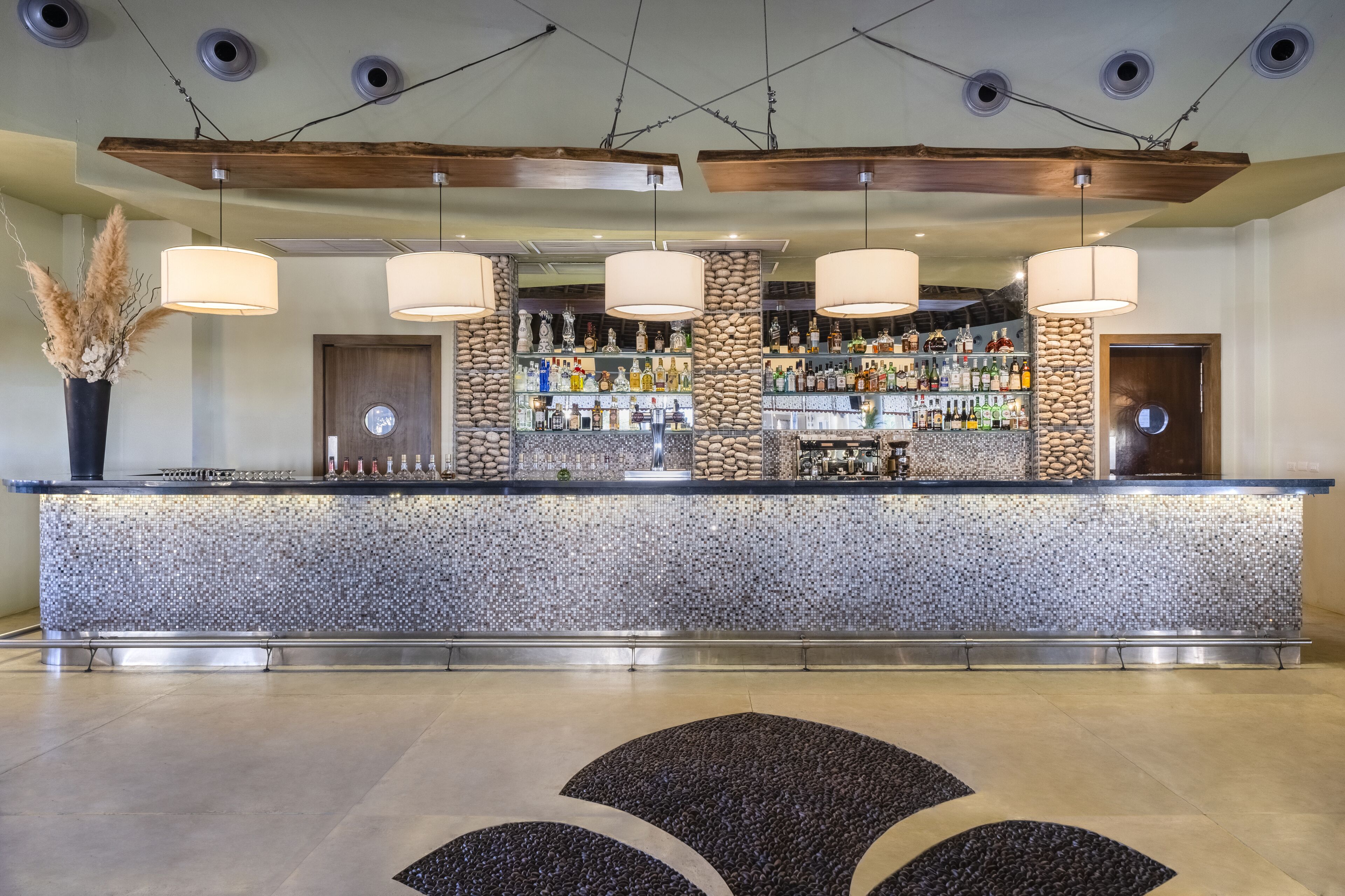 Eine Bar mit einer Steintheke, hängenden Pendelleuchten und einer Auswahl an Flaschen.