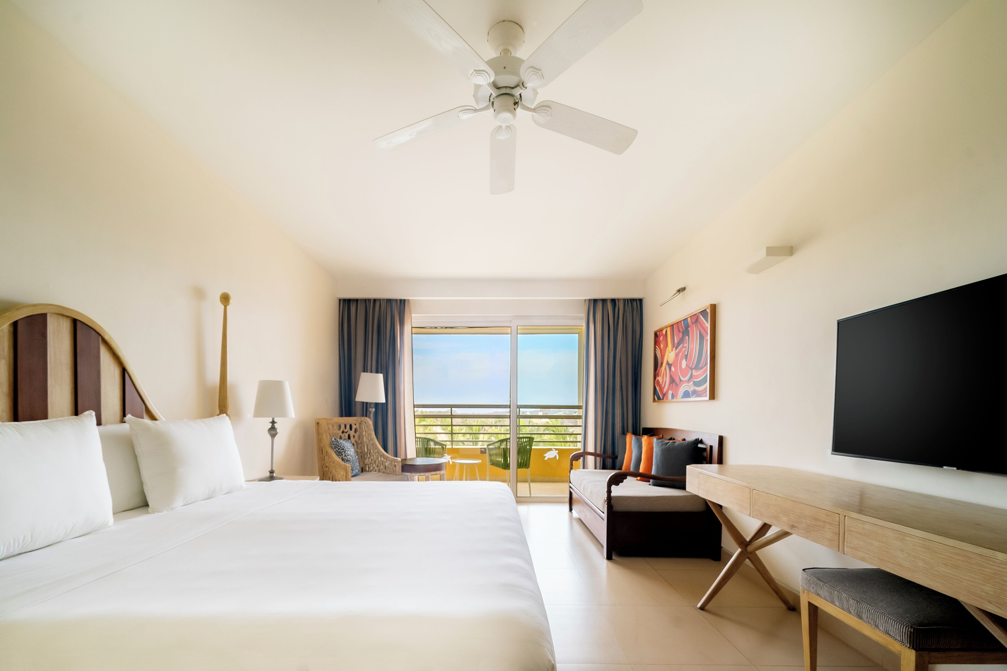 A hotel room with a large bed, a desk, a chair, a TV, and a balcony with a view.