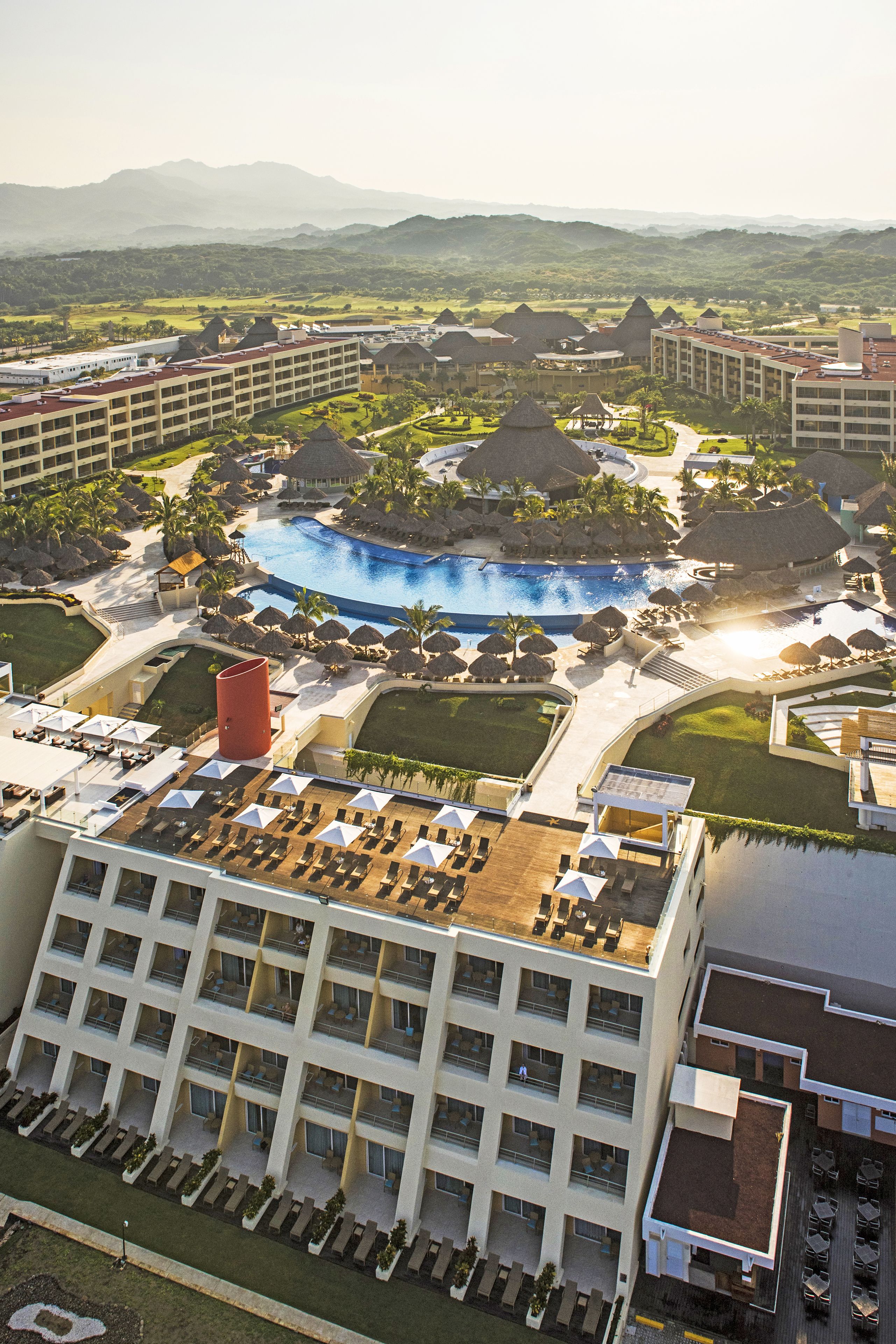 Ein Resort mit mehreren Gebäuden, einem zentral gelegenen Schwimmbad und umgebender Bepflanzung.