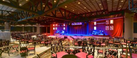 A large indoor auditorium with tiered seating, a stage, and a high ceiling with visible beams.