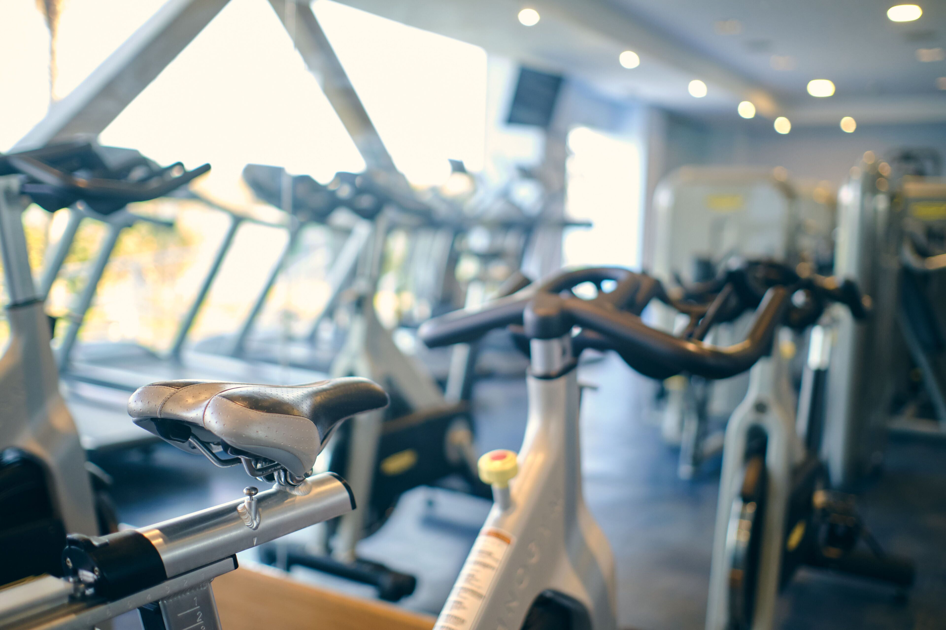 Varias bicicletas estáticas en un gimnasio con amplio ventanal y ambiente luminoso.
