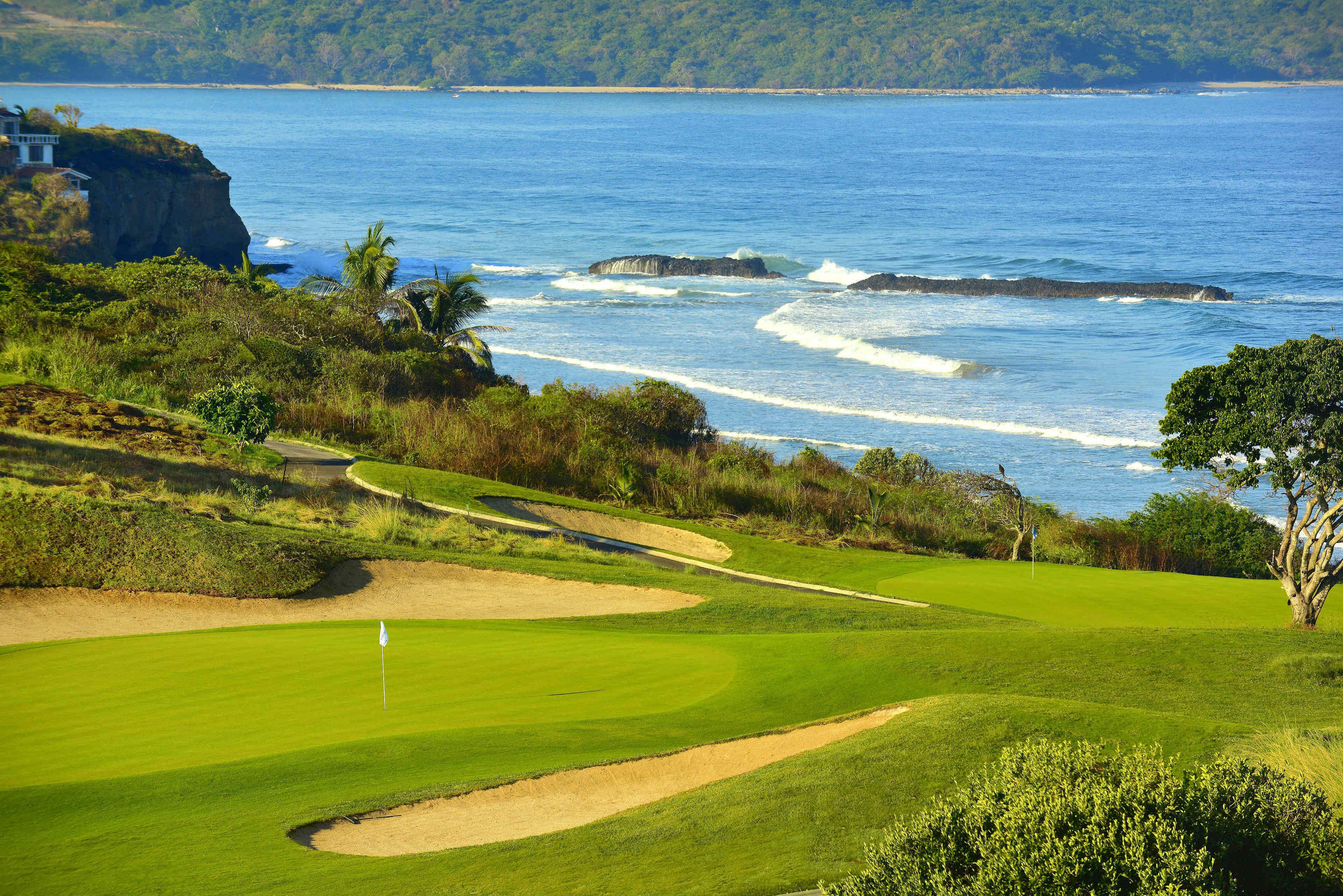 A golf course with a flagstick, sand bunkers, and a view of the ocean.