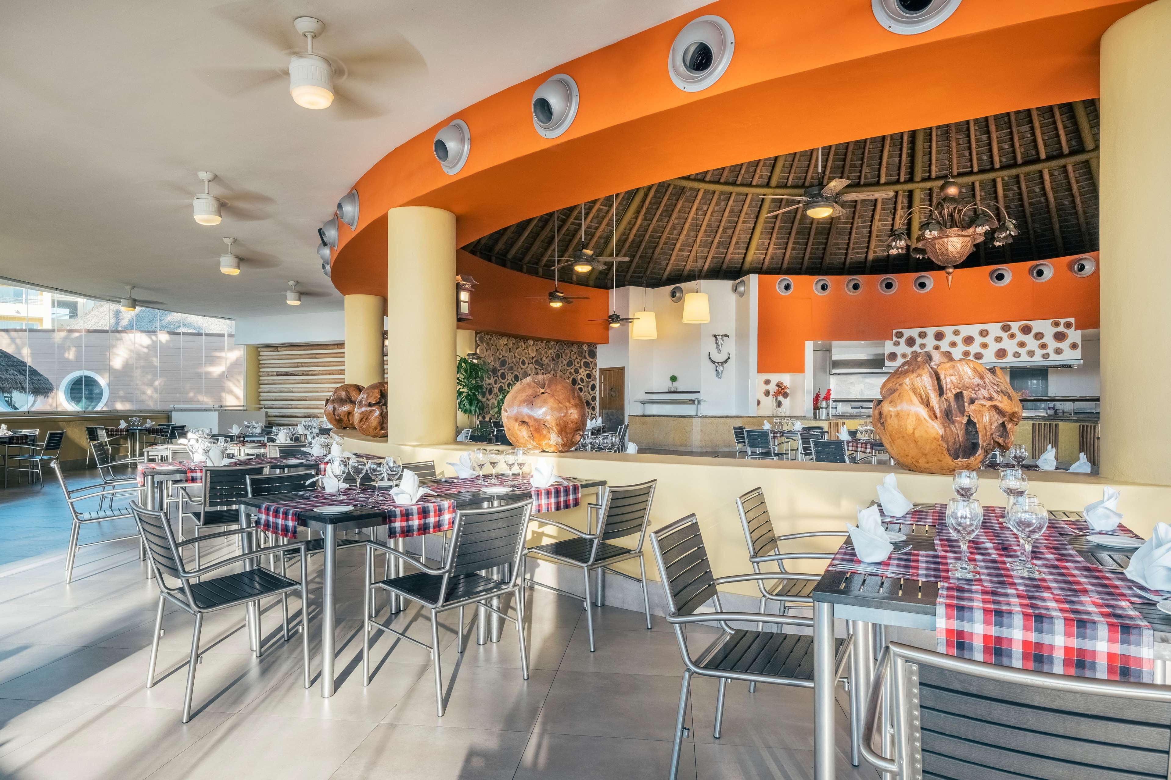 Een restaurant met terras, een centraal eiland met een grote gebraden kip, en een moderne keuken op de achtergrond.
