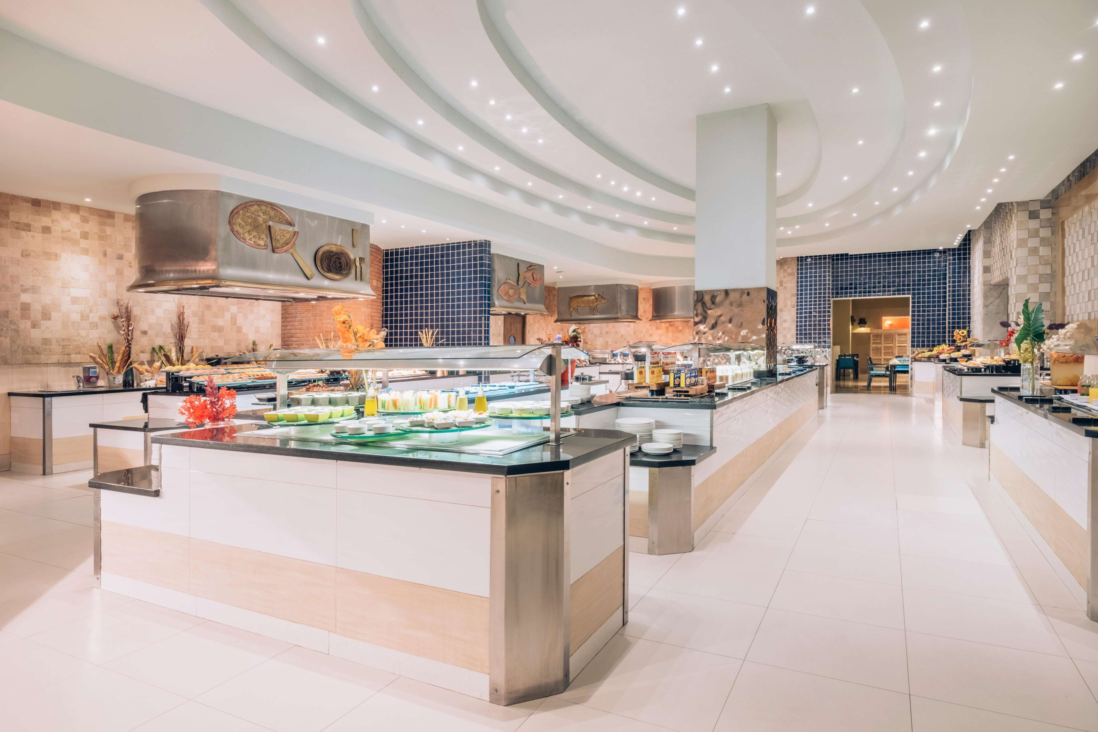 A modern, well-lit kitchen area with a central island, various food stations, and a large, decorative wall.