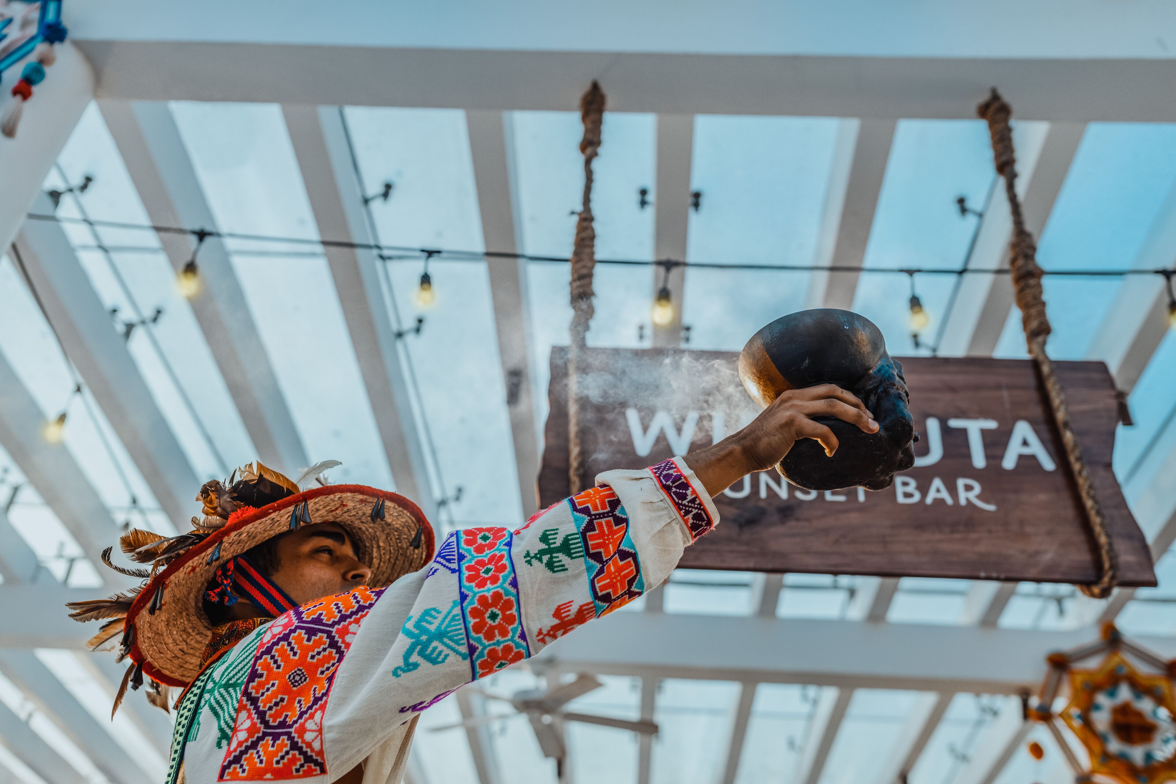 Une personne portant un chapeau traditionnel et tenant un verre dans un bar appelé « WILTON BAR ».