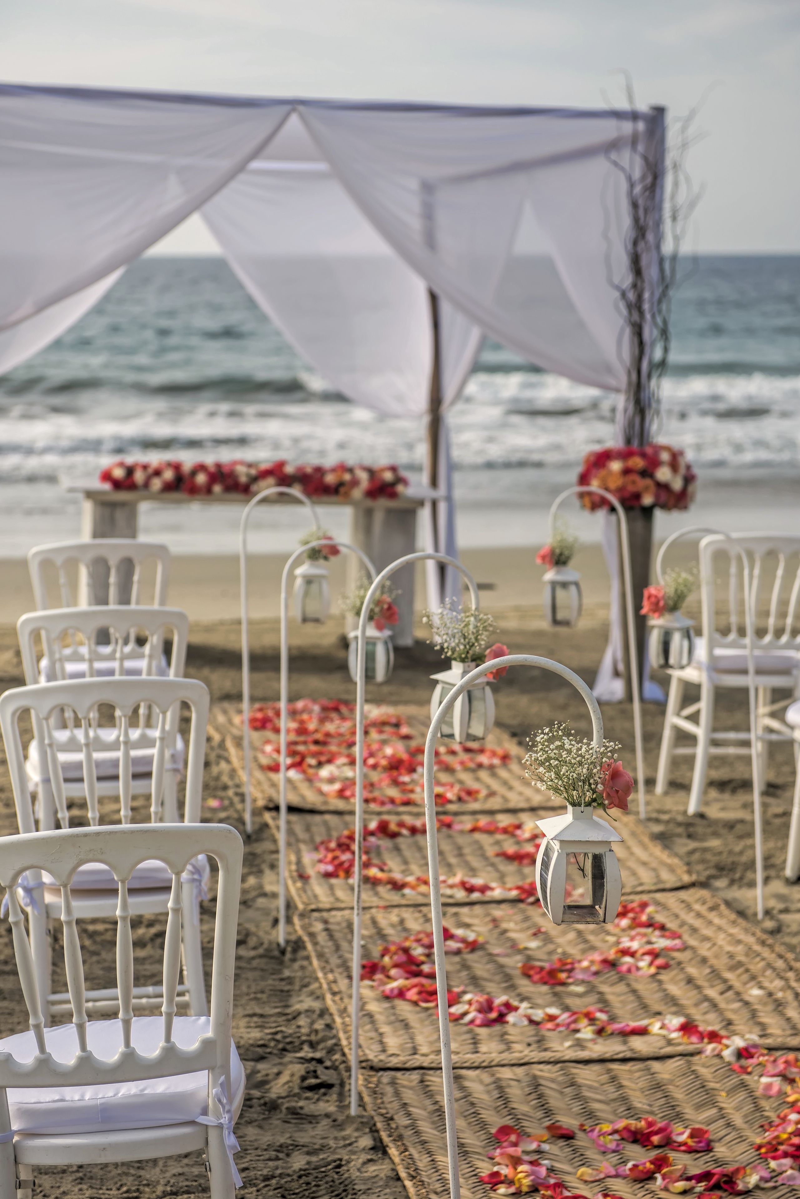 A beach wedding setup with white chairs and a canopy.