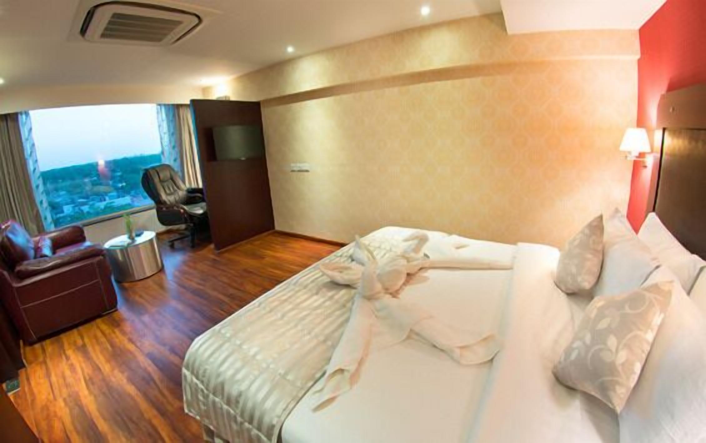 A hotel room with a large bed, a desk, a chair, and a view of the city.