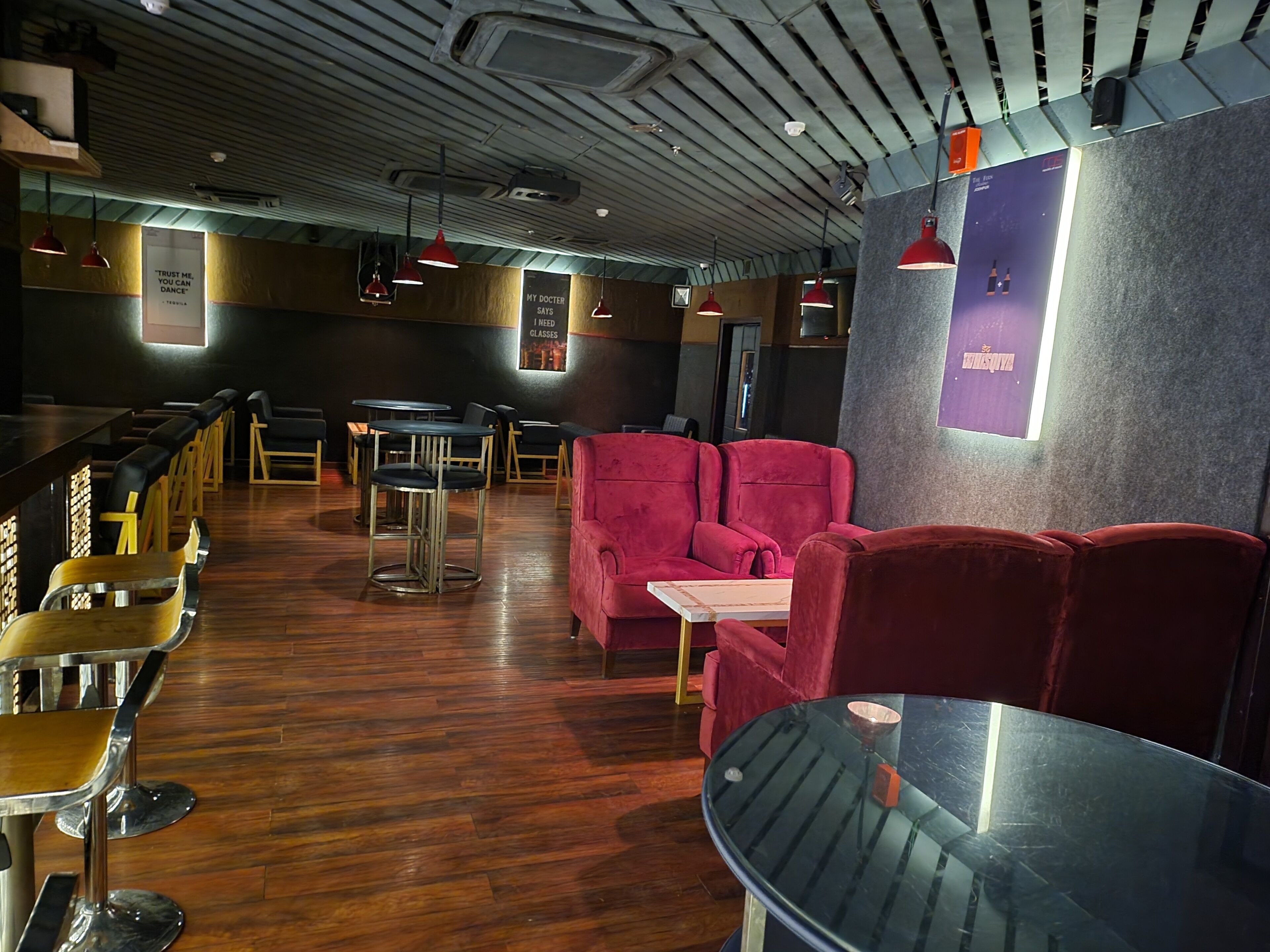 Interior de restaurante con suelo de madera, asientos tapizados en rojo e iluminación colgante.